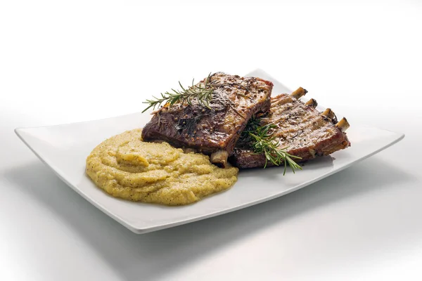 Белая прямоугольная тарелка с запечёнными ребрами свинины и кукурузной кашей — стоковое фото