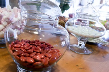 İçinde renkli şekerli badem çeşitleri olan cam kavanozlarla dolu bir masa.