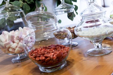 İçinde renkli şekerli badem çeşitleri olan cam kavanozlarla dolu bir masa.