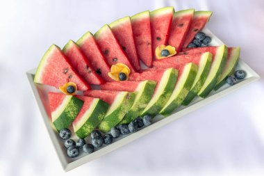Beyaz zemin üzerinde karpuz dilimleri ve yaban mersini dilimleri olan dikdörtgen tepsi