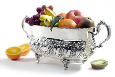 Beyaz arka planda farklı meyveler bulunan gümüş kaplama sepet.