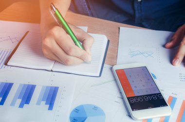 Vade hesaplama ve cep telefonu ile ahşap masa arka planda kaydetme Asya el.