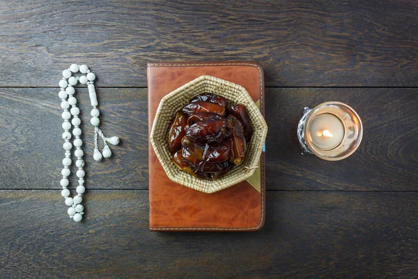 Table top view aerial image of decoration Ramadan Kareem holiday background.Flat lay date in wood basket with white rosary & lighting.The holy book of Koran on modern rustic brown wood at office desk.