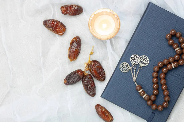 Table top view aerial image of decoration Ramadan Kareem holiday background.Flat lay date with brown rosary & candle lighting.Holy book of Koran on modern rustic white cloth at office desk and space.