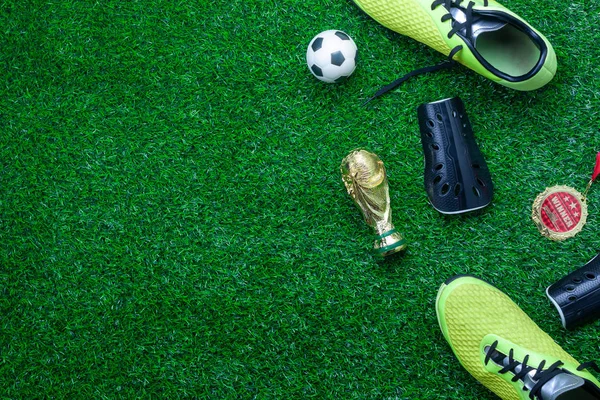 Tablo üst görünümden futbol ya da futbol Dünya Kupası sezon arka plan. Düz yatıyordu aksesuarları kupa ve yapay yeşil çim duvar kağıdı üzerinde ayakkabı ile top. Yaratıcı tasarım metin ve içerik için boş alan.
