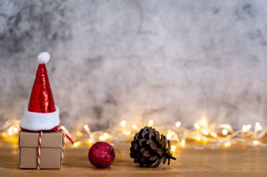 Mutlu Noel süslemeleri ve Mutlu Yeni Yıl süslemeleri aksesuarları. Noel Baba şapkalı hediye kutusu, modern kırsal kahverengi ve gri renkli ışıklandırmalı arkaplanda parti sezonuna itiraz ediyor..