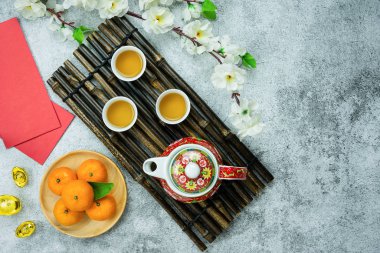 Çince zengin, varlıklı ve mutlu anlamına gelir. Çin Yeni Yıl Tatili konseptinin arka planı. Pembe kiraz çiçeği ve gri çimento üzerinde altın içeren taze portakal ve fincan çay..