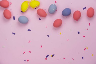 Düzenleme dekorasyonunun en üst görüntüsü Mutlu Paskalya bayramı arka plan kavramı. Düz, ofis masasındaki modern pembe kağıdın üzerine aksesuar konfetiyle renkli tavşan yumurtaları serer. Pastel tonunu tasarla..