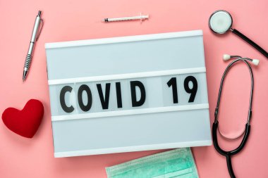 Coronavirus veya COVID-19 metin arkaplan konsepti ile aksesuarların hava görüntüsü. Pembe kağıt üzerinde yüz maskeli düztabaka kalp ve teleskop ve şırınga..