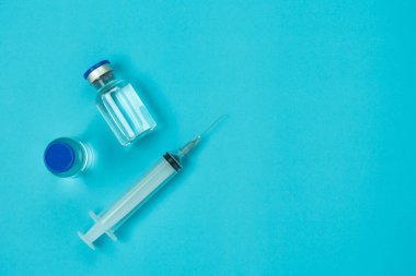 Üst tabaka sağlık aksesuarları ve koronavirüs arka plan kavramına sahip tıbbi aksesuarlar. Mavi kağıdın üzerinde şırınga bulunan anti-retroviral aşı şişesi. Hasta Covid-19 'u tedavi eden doktor için düz eşyalar yatıyordu..