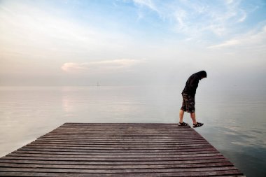 Depresif genç adam tahta köprüden aşağı bakıyor deniz genişletilmiş tutuyoruz