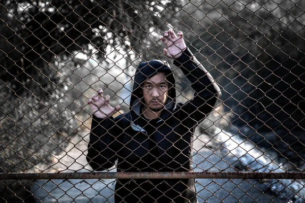 Homem de pé atrás de uma cerca mão agarra gaiola de malha de aço — Fotografia de Stock