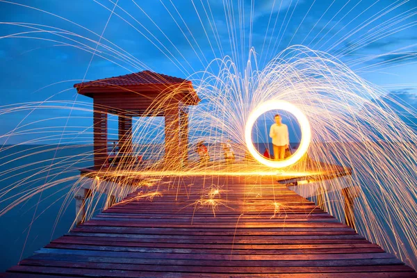 Man Spinning Burning Steel Wool on Wooden Bridge Extended into the Sea