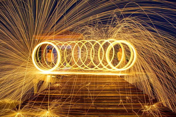 Man Spinning Burning Steel Wool on Wooden Bridge Extended into the Sea