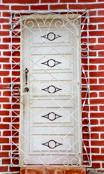 Pas geschilderde witte deur achter rooster op verse bakstenen muur — Stockfoto
