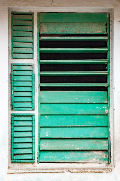Gedeeltelijk open afgestoken groene luiken in venster op de witte muur — Stockfoto