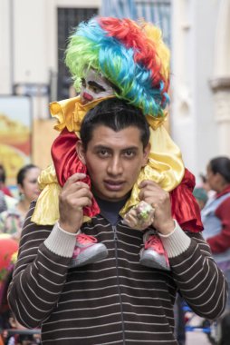 Cuenca, Ekvador - 24 Aralık 2015 - Genç baba oğlunu palyaço kılığında omuzlarında tutuyor