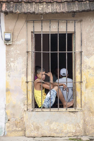 Rapaz senta-se na soleira da janela atrás de barras de ferro olhou para a rua — Fotografia de Stock