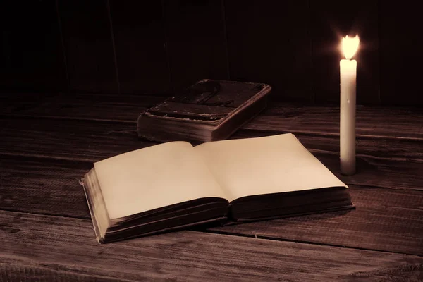 Viejo libro antiguo abierto con vela encendida cerca de la mesa de madera. Página en blanco —  Fotos de Stock