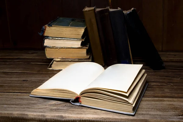 Antiguos libros antiguos abiertos en una mesa de madera en el fondo de un montón de libros . —  Fotos de Stock