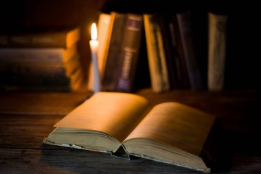 Boş sayfaları ile açık bir kitap diğer ayakta kitap ve yanan mum arka plan üzerinde ahşap bir masa üzerinde yatıyor.