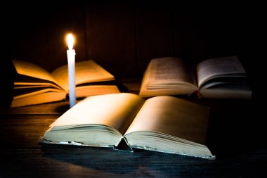 Boş sayfaları ile açık bir kitap diğer ayakta kitap ve yanan mum arka plan üzerinde ahşap bir masa üzerinde yatıyor.