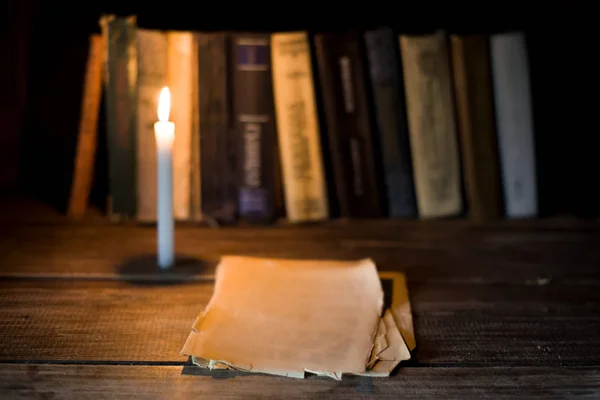 Several sheet of blank papers lies on a wooden table on the background of standing books and burning candle. — Stock Photo, Image