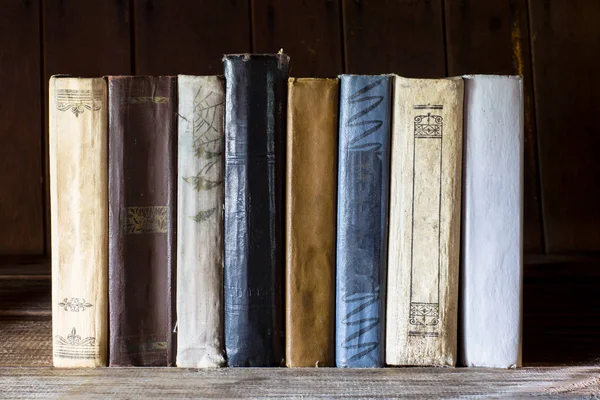 Old books stand in row on wooden table. The back of the books is facing the viewer.