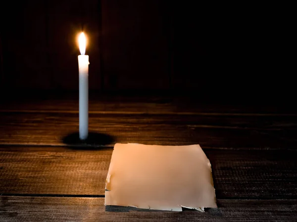 Hoja de papel en blanco se encuentra en una mesa de madera con vela encendida . —  Fotos de Stock