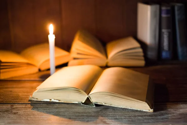 Een open boek met lege pagina's ligt op een houten tafel op de achtergrond van de andere geopende boeken en brandende kaars. — Stockfoto