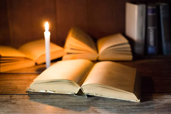 Un libro abierto con páginas en blanco yace sobre una mesa de madera en el fondo de otros libros abiertos y velas encendidas . Imagen de archivo