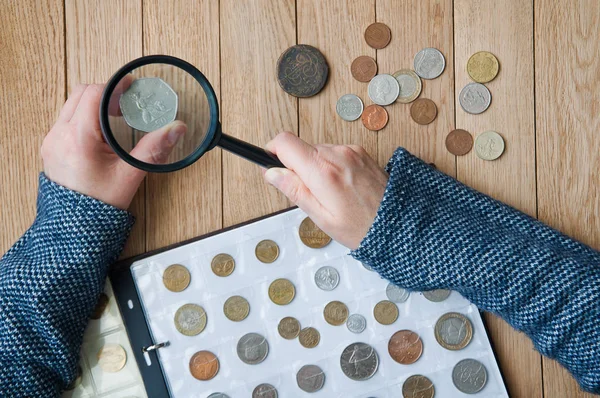 Mujer-numismático ve monedas de un álbum de monedas a través de una lupa —  Fotos de Stock