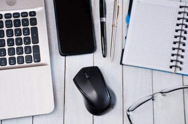 Laptop with mouse, smartphone, notebook, pens and glasses on whi