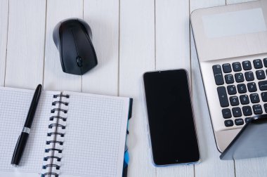 Laptop with mouse, notebook, pen and smartphone on white wooden 