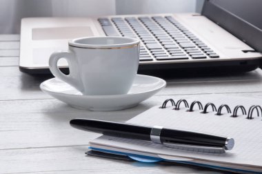 Cup of coffee, laptop and notebook with pen on desktop