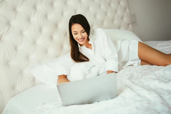 Beatufiul morena usando laptop na cama — Fotografia de Stock