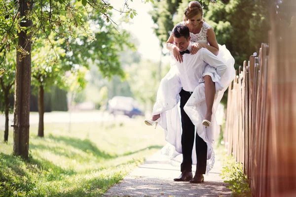 Brudgummen bär bruden piggyback — Stockfoto