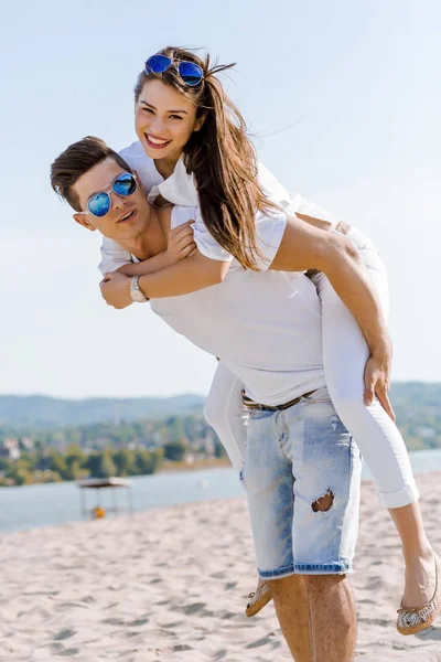 Cheerful handsome man carrying his girlfriend piggyback — Stock Photo, Image