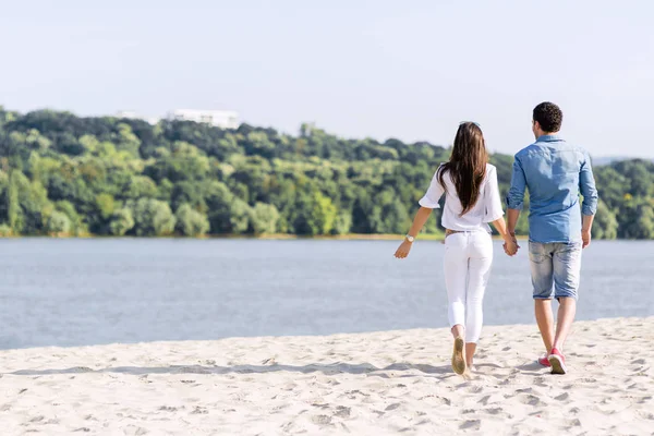 Pareja cogida de la mano y caminando en una playa — Foto de Stock