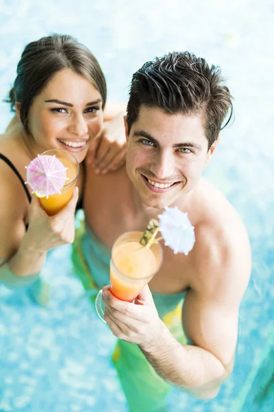 Retrato de una pareja sonriendo y bebiendo un cóctel en una piscina — Foto de Stock