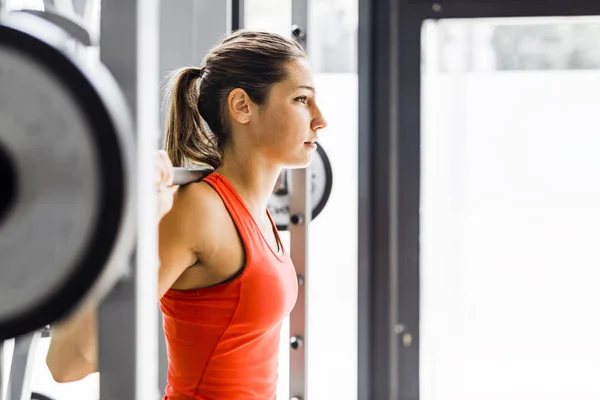 Joven hermosa mujer levantando pesas en un gimnasio — Foto de Stock