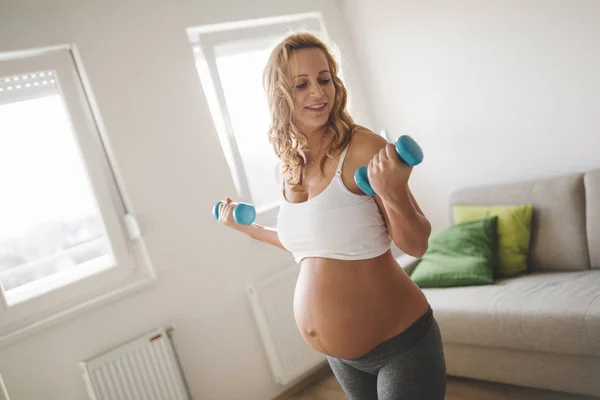 Беременная женщина тренируется с гантелями — стоковое фото