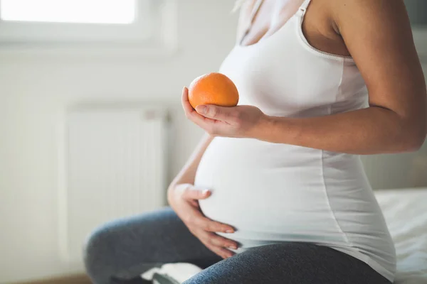Беременная женщина держит в руке оранжевый — стоковое фото