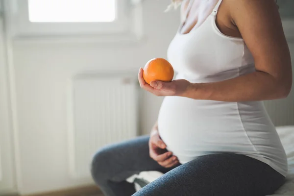 Mulher grávida segurando laranja na mão — Fotografia de Stock