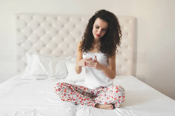 Yatakta otururken telefon kullanan kadın — Stok fotoğraf