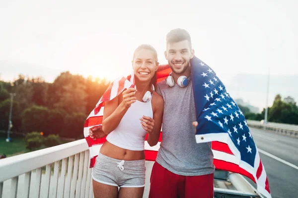 Portrait of attractive fitness couple holding American flag — Stock Photo, Image