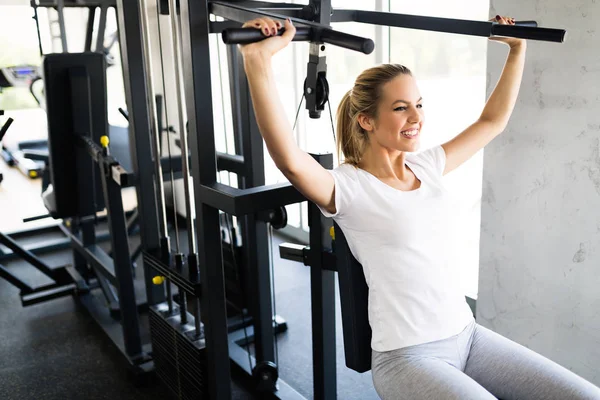 Jeune femme travaillant dans la salle de gym sur la machine de presse épaule — Photo