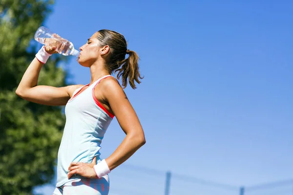 Junge schöne Athletin trinkt Wasser nach dem Training — Stockfoto