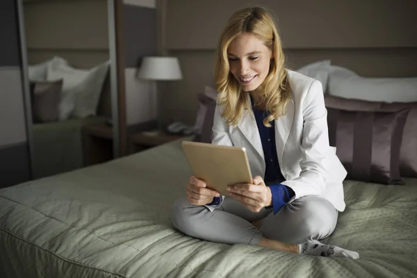 Portrait of beautiful businesswoman sitting on bed and using tablet