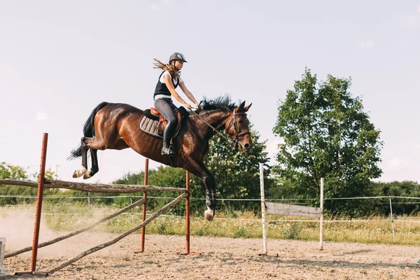 Jovem jóquei do sexo feminino no cavalo pulando sobre obstáculo — Fotografia de Stock